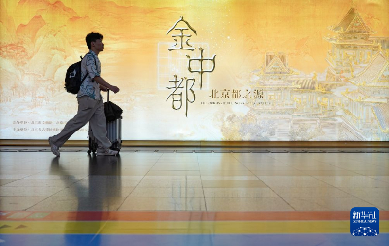 7月30日、特別展「金中都——北京都之源」の大型ディスプレイの前を横切る旅客。