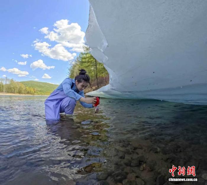 「中国で最も寒い村」に現在もまだ残っている氷の層の写真を撮影する女性（画像提供・呼中区党委員会宣伝部）。